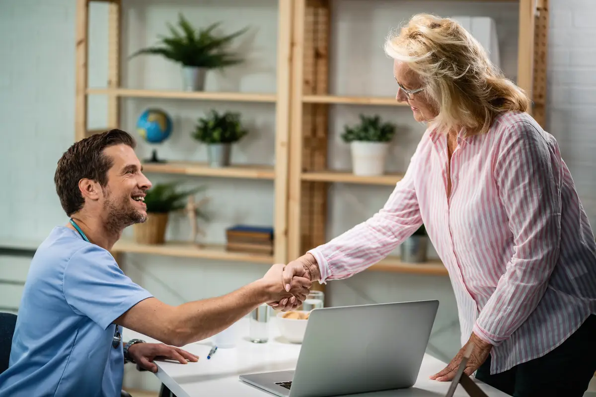 Happy doctor shaking hands with senior woman who came to medical appointment
