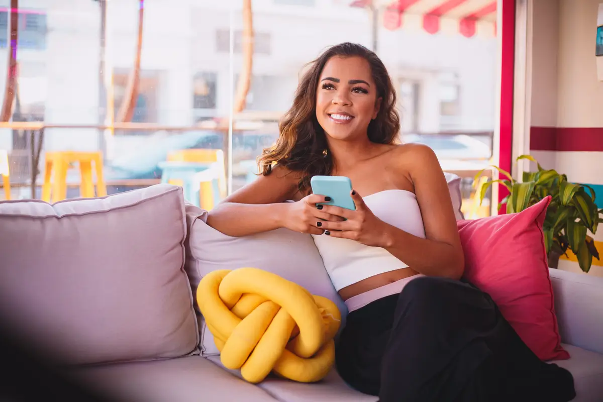 Young afro woman sitting on sofa using cellphone at home