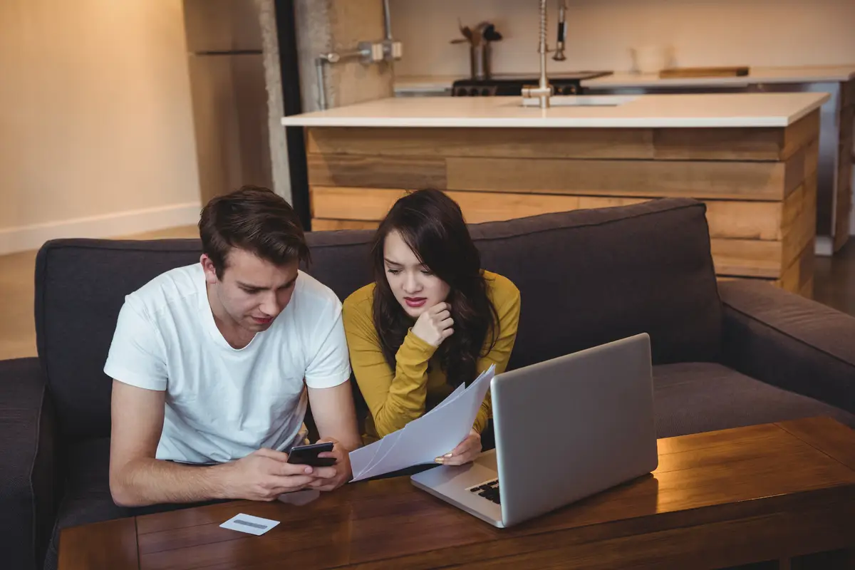 Couple sitting on sofa discussing with financial documents in living room