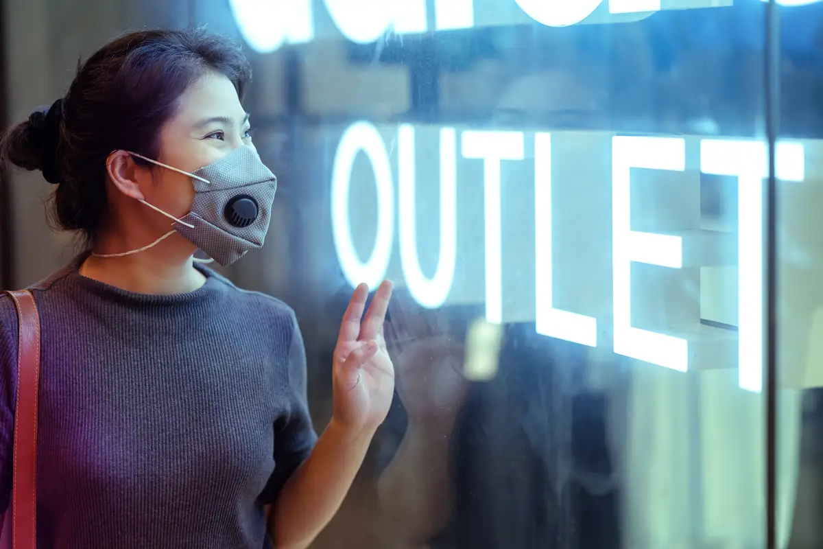 Cheerful attractive asian female woman wearing protective face mask looking at outlet sale signage shopfront window display new normal lifestyle concept