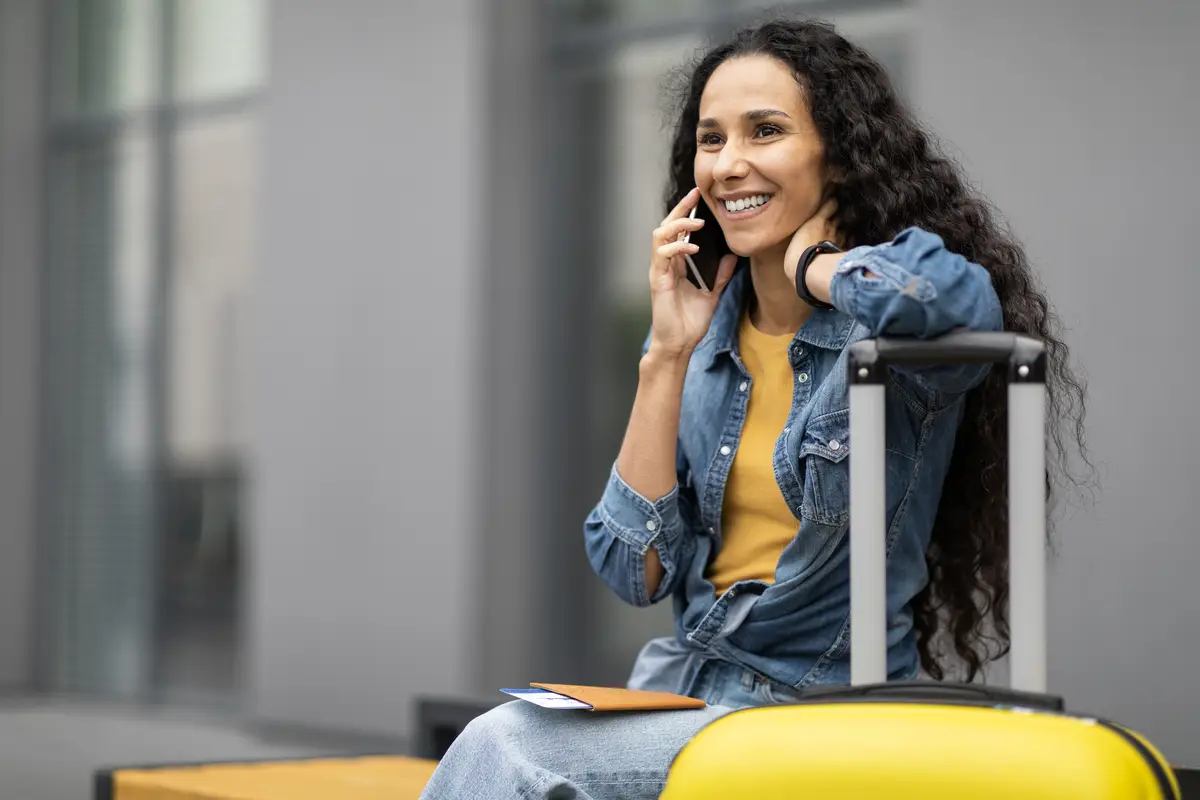 Positive young woman tourist sitting on bench having phone conversation