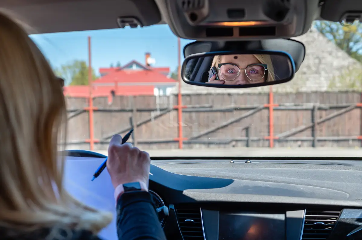 Middle-aged woman in glasses in the car working with documents and talking on the phone rear view
