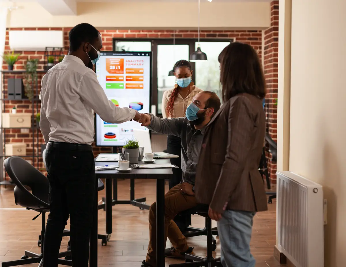 Businesspeople wearing medical face mask doing fist bump gesture to prevent infection with coronavirus before start working at company presentation in startup office. Business concept