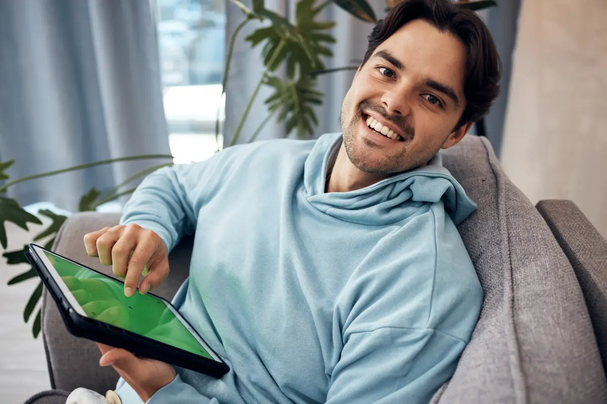 Portrait tablet and green screen with a man gaming on a sofa in the living room of his home to relax Technology smile and happy young gamer using a display with tracking markers in his apartment