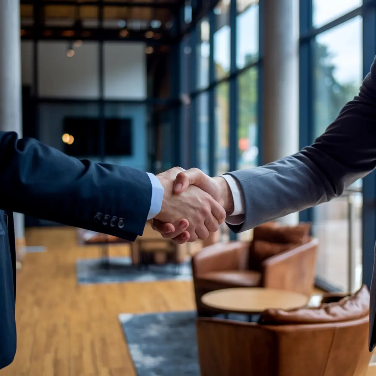 Aperto de mãos entre duas pessoas vestindo ternos em ambiente corporativo moderno