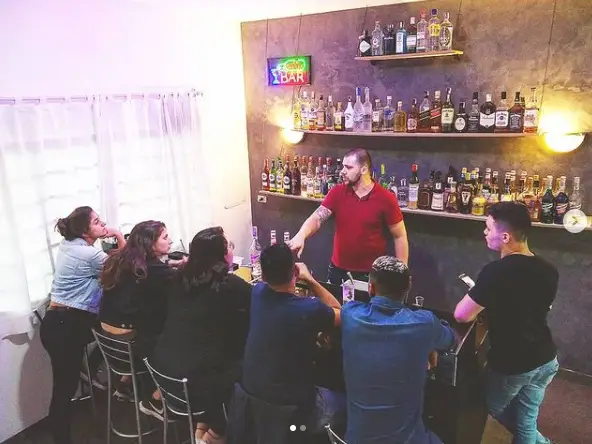 Aula prática de bartender com instrutor explicando para estudantes no bar da escola LuxBar