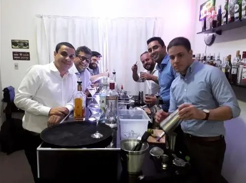 Grupo de seis homens em aula prática de bartender preparando coquetéis em bar de escola no Tatuapé