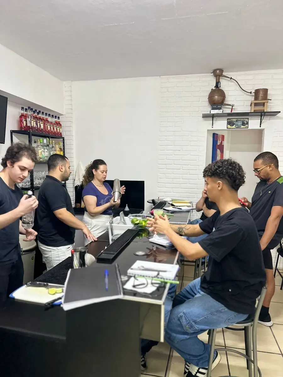 Aula prática de bartenders com grupo de alunos aprendendo a preparar drinks em bar interno