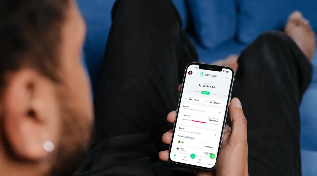 Pessoa usando smartphone com aplicativo moneey aberto na tela mostrando saldo e finanças