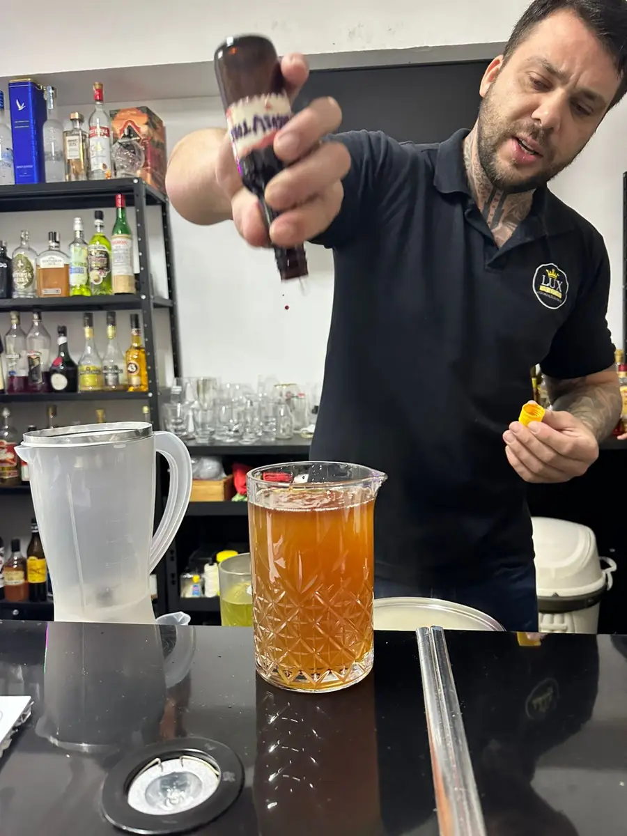Bartender adicionando gotas de líquido em jarra com bebida âmbar em balcão de bar
