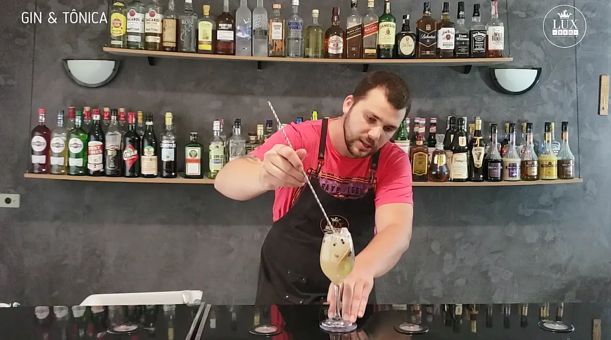 Bartender mexendo drinque de gin tônica com colher bailarina em bar moderno