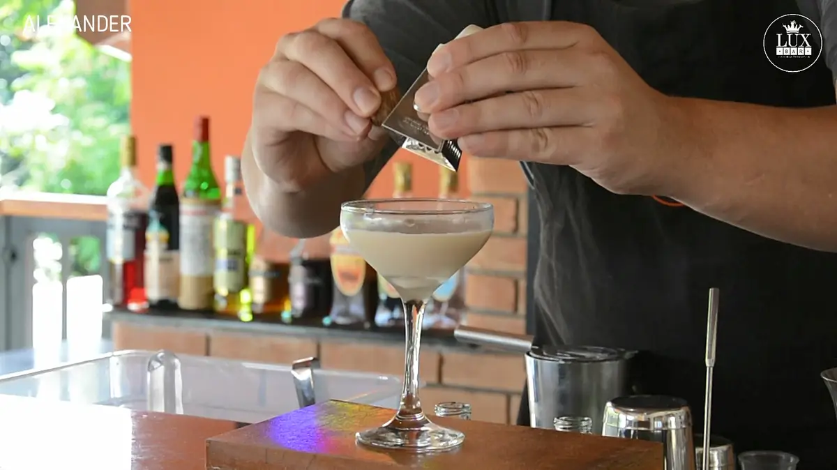 Bartender polvilhando especiarias em drink cremoso em taça de coquetel