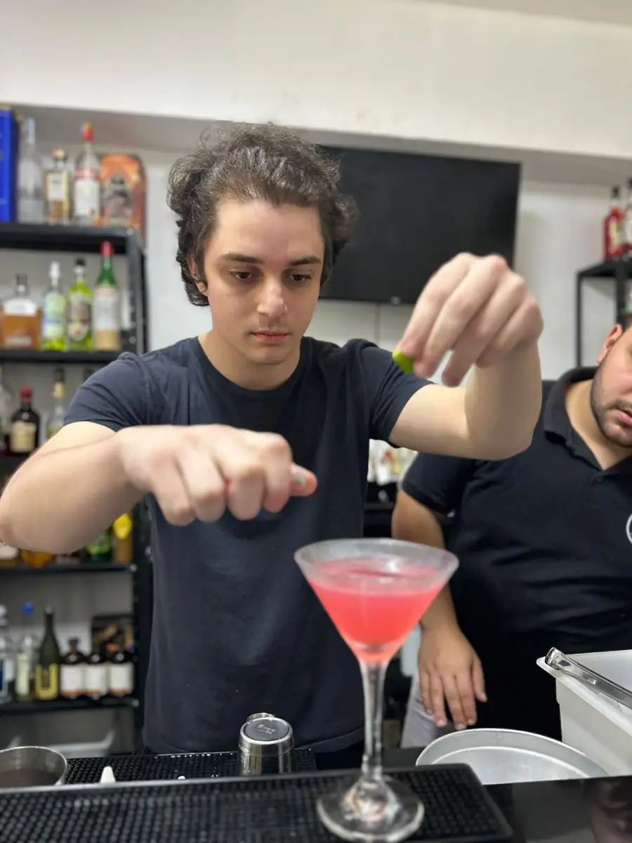 Bartender jovem adicionando guarnição em drink rosa em copo de coquetel.