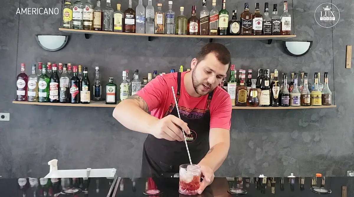 Bartender mexendo um drink vermelho em um copo com gelo no bar da escola LuxBar em São Paulo