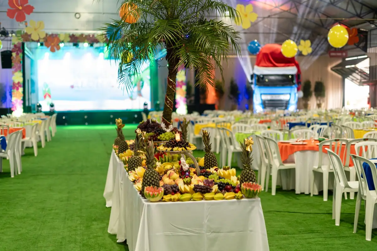 Mesa de buffet decorada com frutas frescas e palmeira no centro de evento corporativo