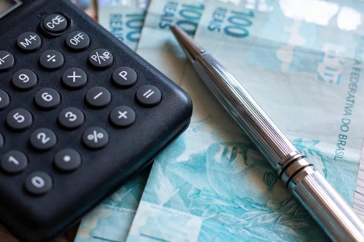 Calculadora preta e caneta metálica sobre notas de cem reais