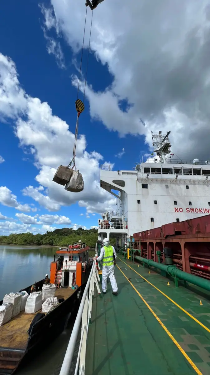 Worker guiding cargo hoisted by crane onto ship deck