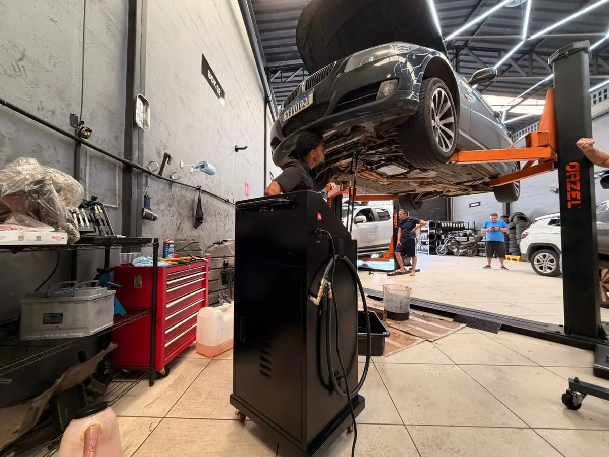 Carro preto elevado em elevador hidráulico em oficina automotiva com mecânico trabalhando embaixo
