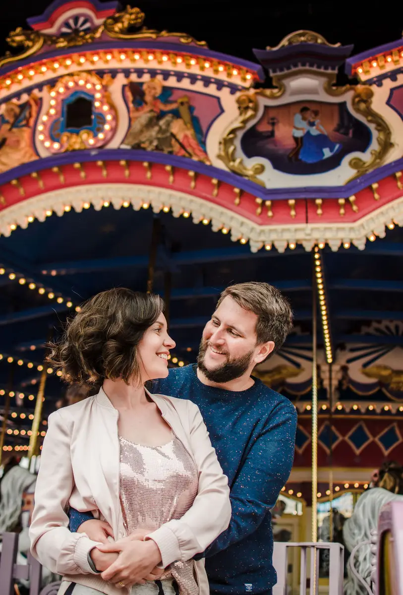 Casal sorridente abraçado na frente de um carrossel iluminado à noite