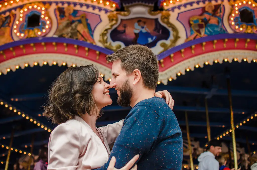 Casal sorridente se abraçando em frente a um carrossel iluminado à noite