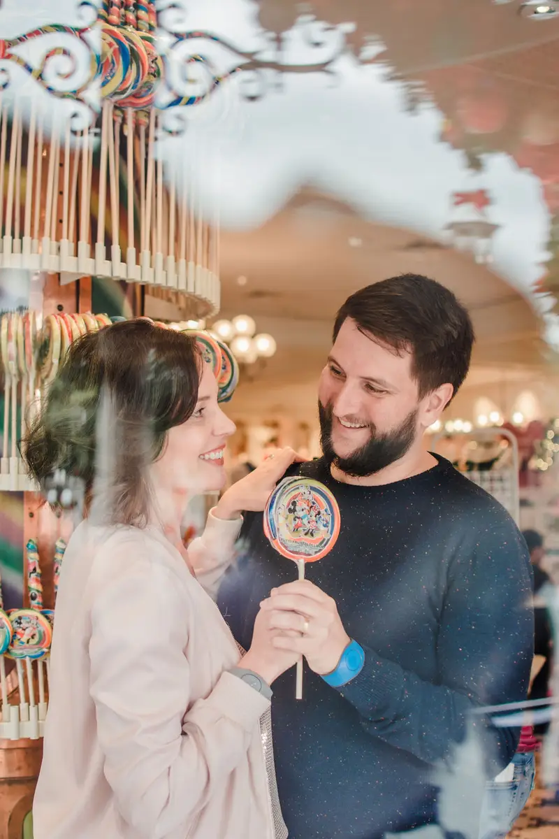 Casal sorrindo e segurando pirulito colorido dentro de loja