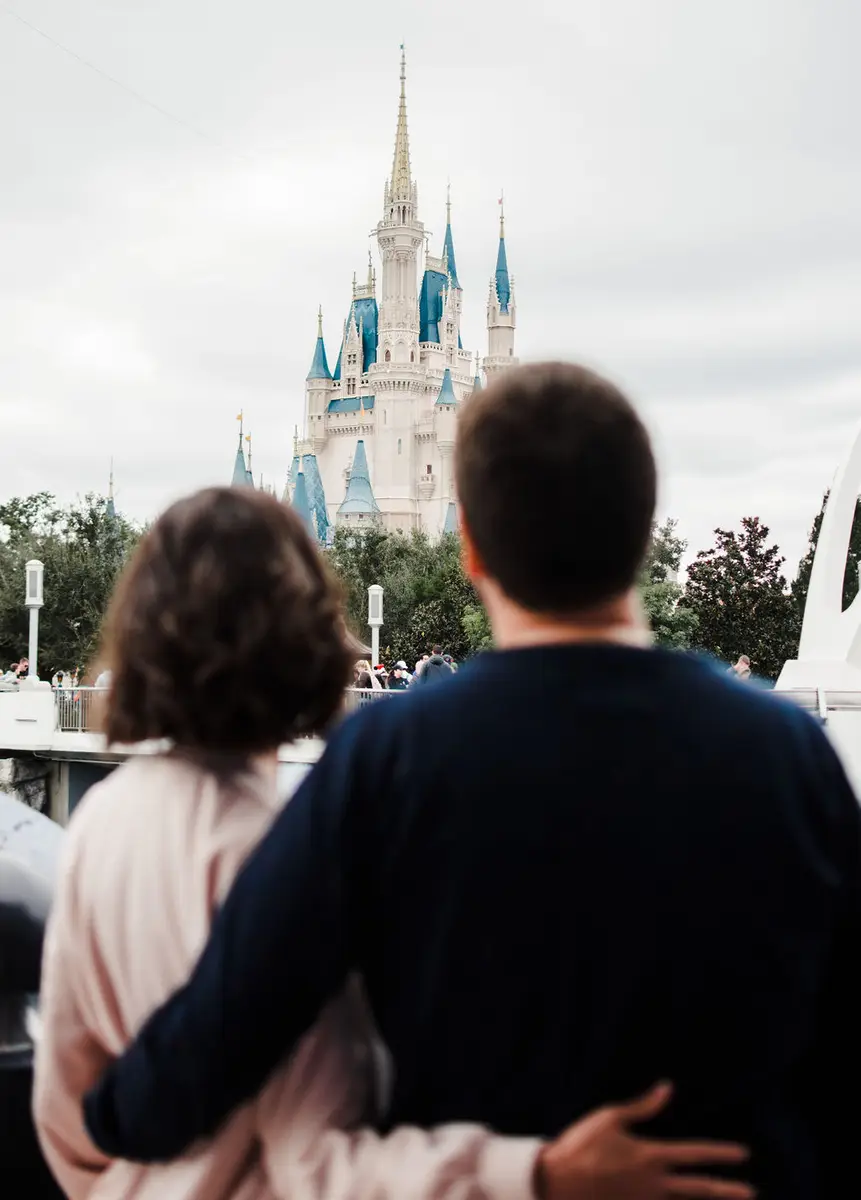 Casal de costas abraçado olhando para o castelo da Cinderela na Disney em dia nublado