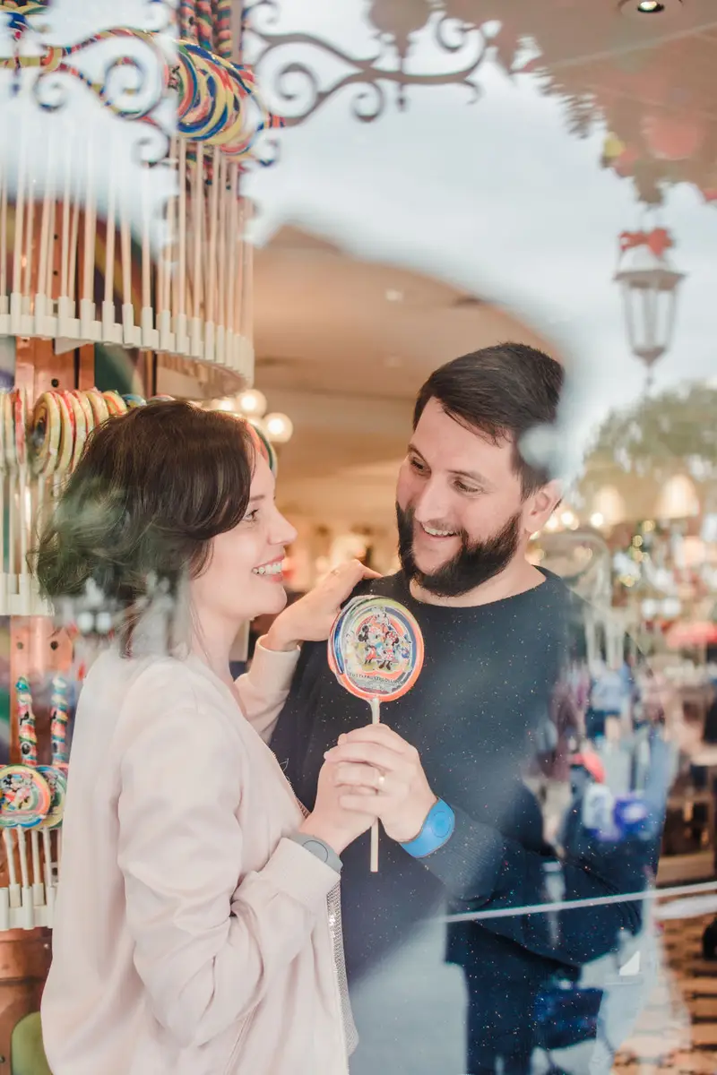 Casal sorri olhando um para o outro segurando um pirulito colorido em loja de doces