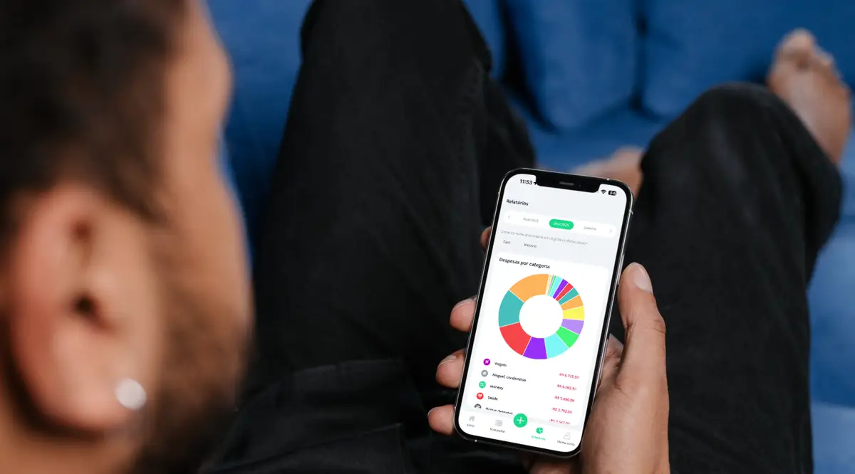 Pessoa segurando celular com gráfico de pizza colorido de despesas por categoria na tela
