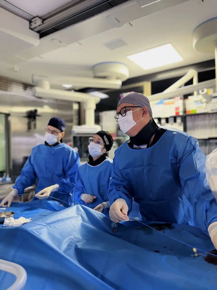 Dr. Marcelo Mandelli e equipe em cirurgia vascular minimamente invasiva com trajes azuis e máscaras em sala cirúrgica