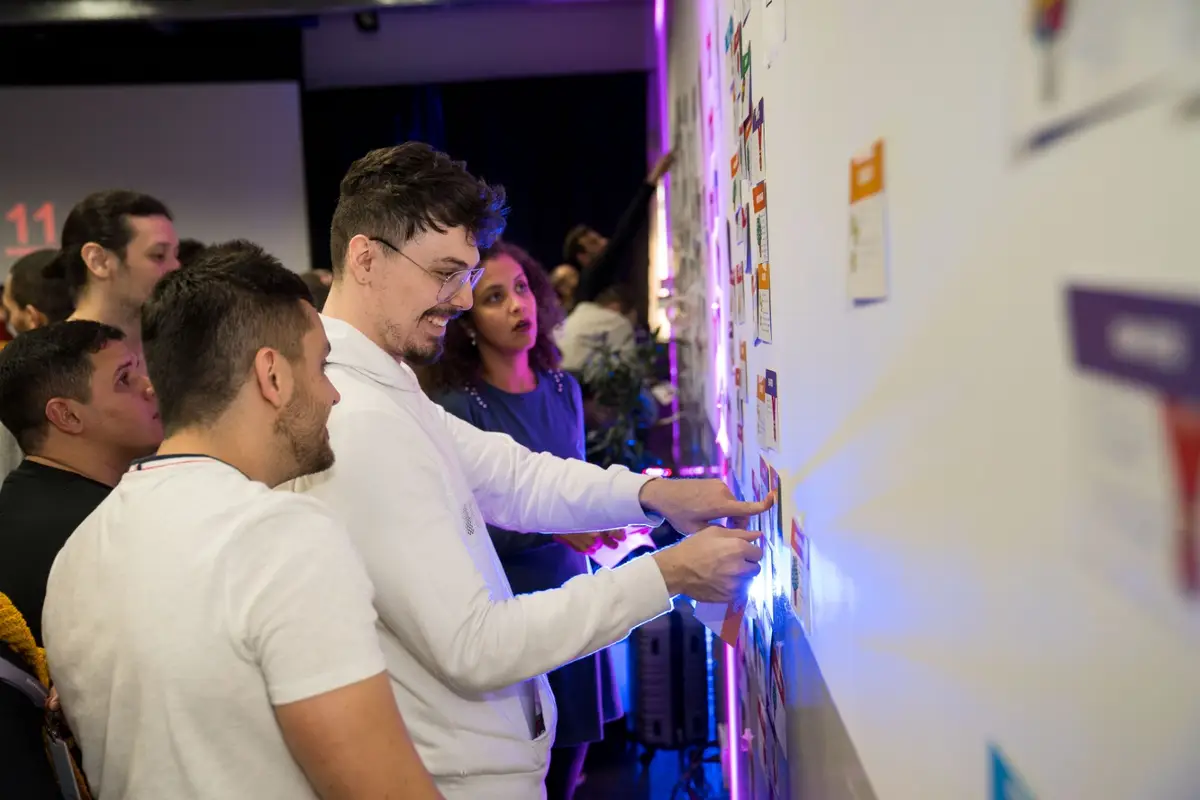 Grupo de pessoas colaborando em quadro branco com notas coloridas em evento interno