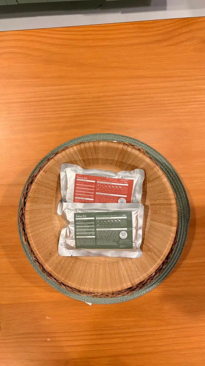 Pacotes de comida natural para cães da Natua Pet em uma tigela de madeira sobre uma mesa de madeira clara