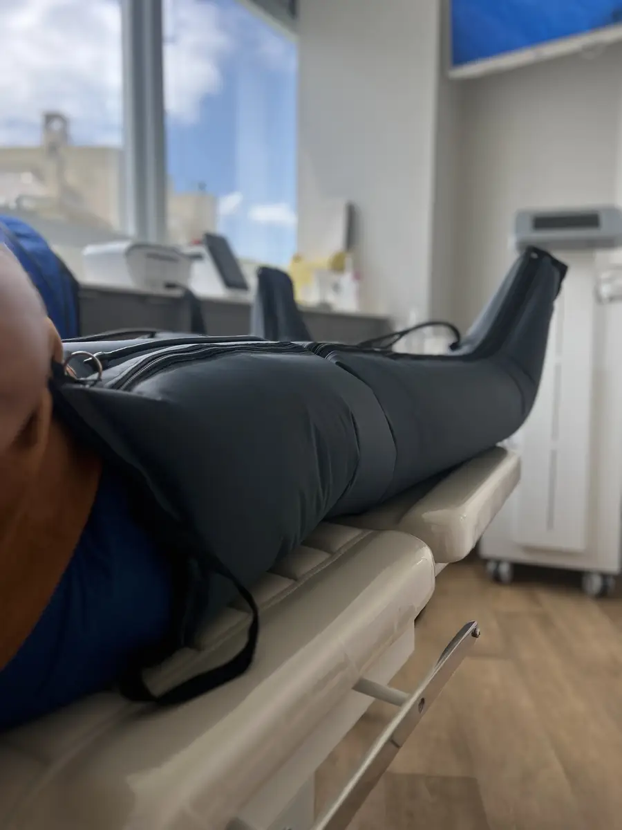 Pessoa deitada com perna envolta em aparelho de compressão pneumática em clínica, bota pneumática