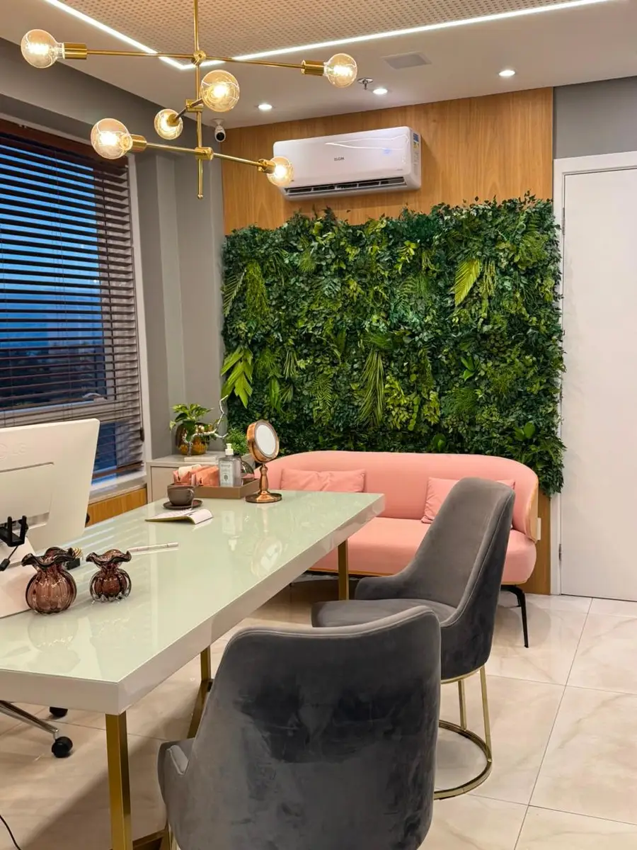 Consultório elegante com mesa branca, cadeiras cinza, sofá rosa e parede verde decorativa