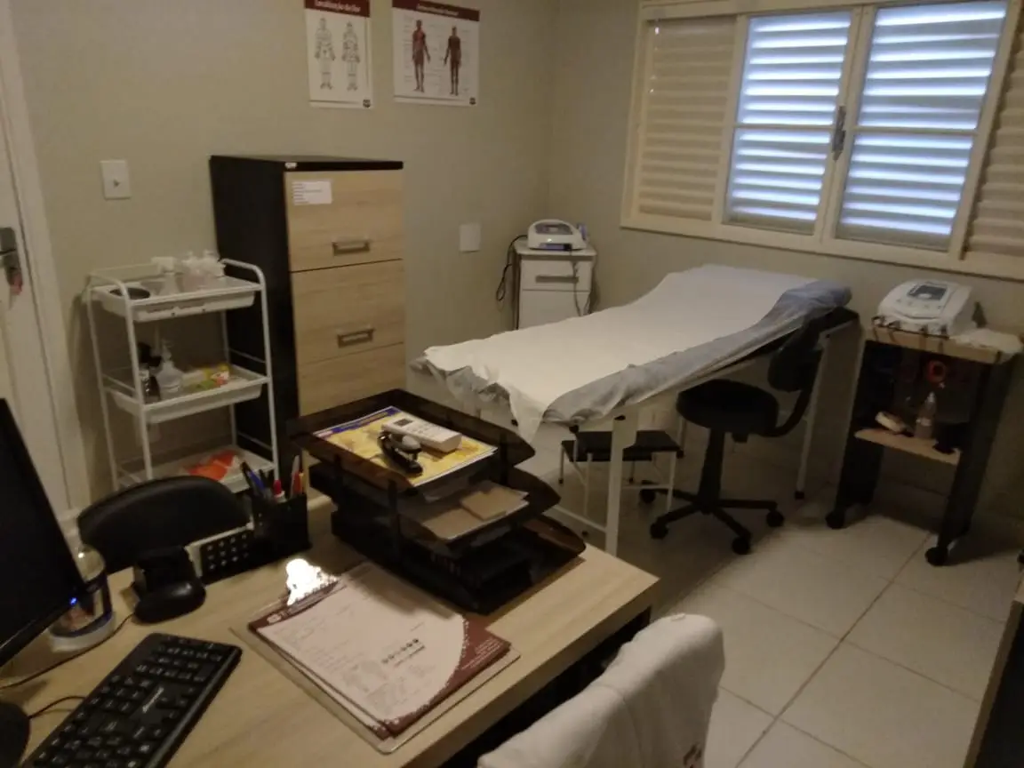 Consultório médico com mesa de trabalho e maca coberta com lençol branco