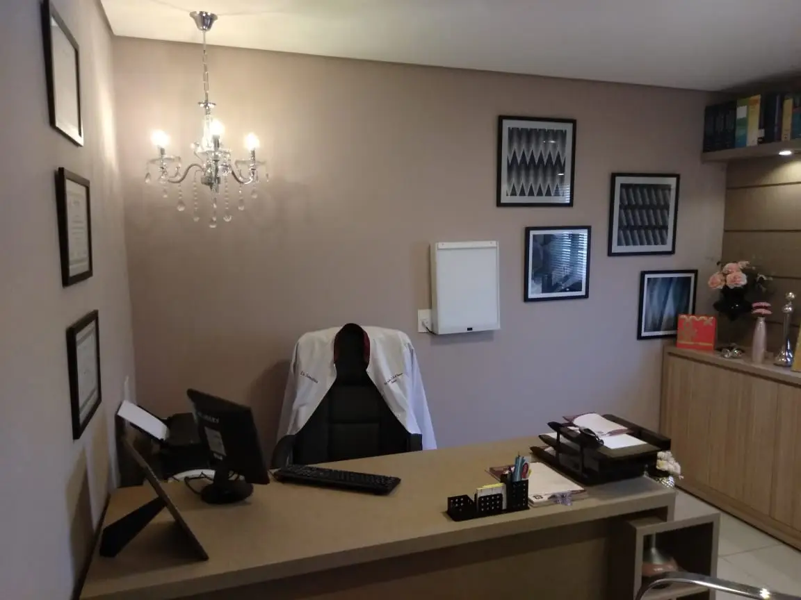 Consultório médico moderno com mesa, cadeira para o profissional, computador e decoração acolhedora