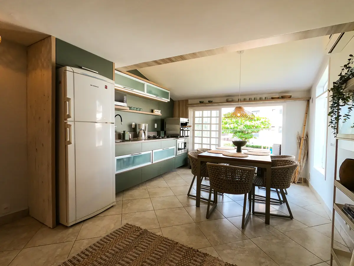 Cozinha e área de jantar com mesa de madeira e cadeiras de vime em ambiente iluminado