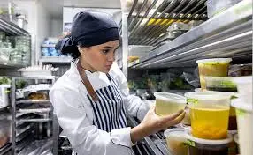Cozinheira organizando potes de alimentos na cozinha de restaurante