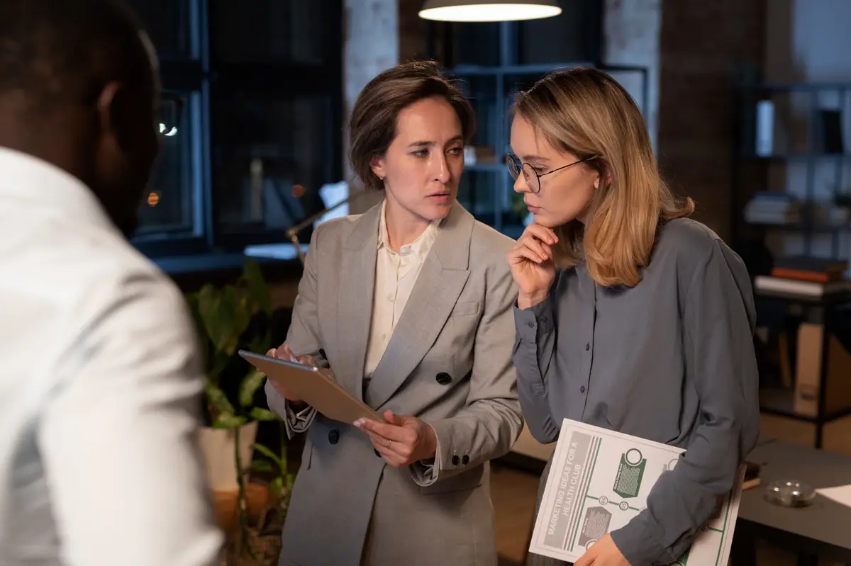 Duas mulheres discutem documentos em escritório à noite