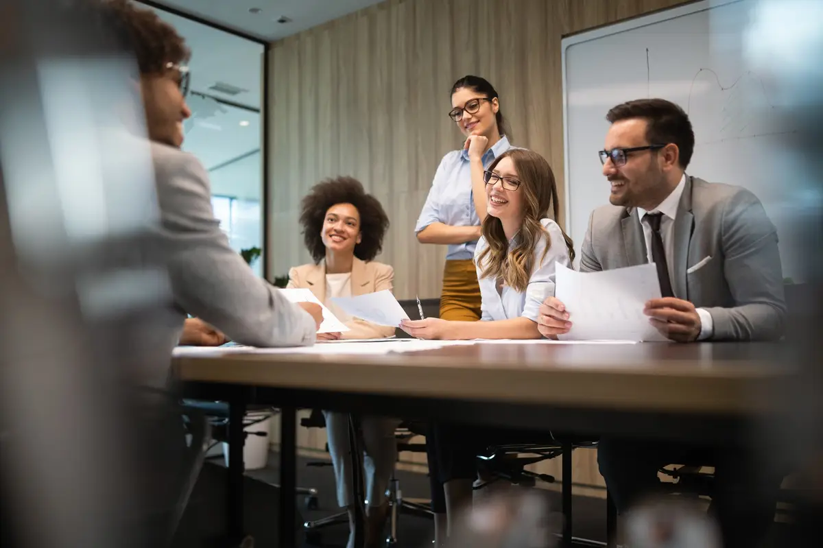 Equipe de quatro pessoas sorrindo e discutindo documentos em sala de reunião