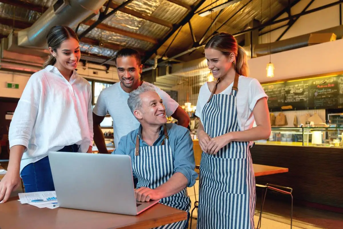 Equipe em restaurante reunida ao redor de laptop para analisar dados de vendas