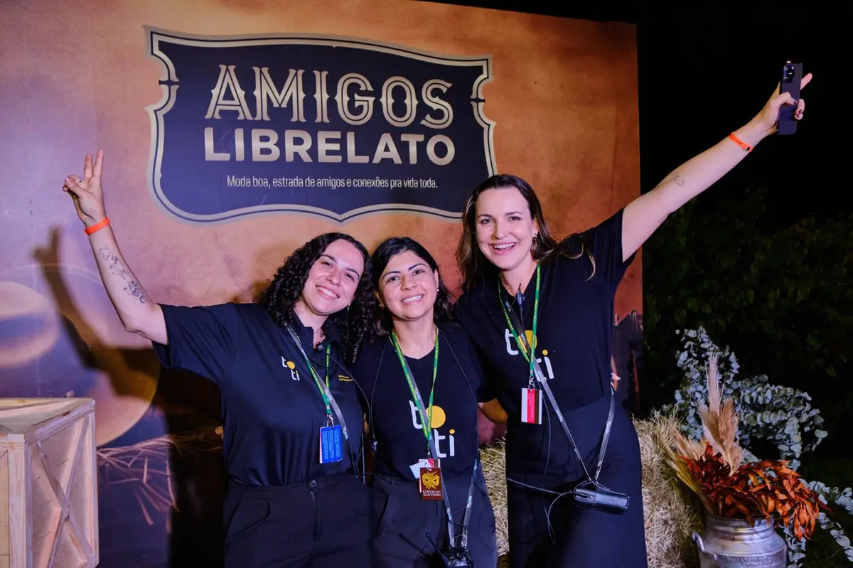 Três mulheres sorrindo vestindo camisetas pretas da Toti Agência em evento Amigos Librelato