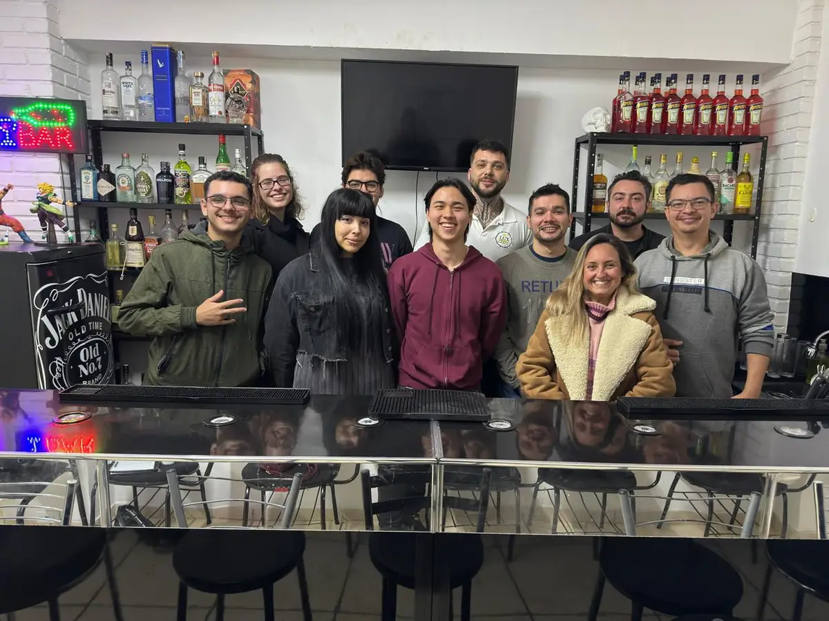 Grupo de dez pessoas em pé atrás do balcão de bar em uma escola de bartenders.