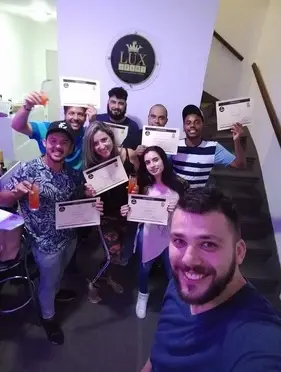 Grupo de oito pessoas segurando certificados e copos com drinks posando para foto em escola de bartenders