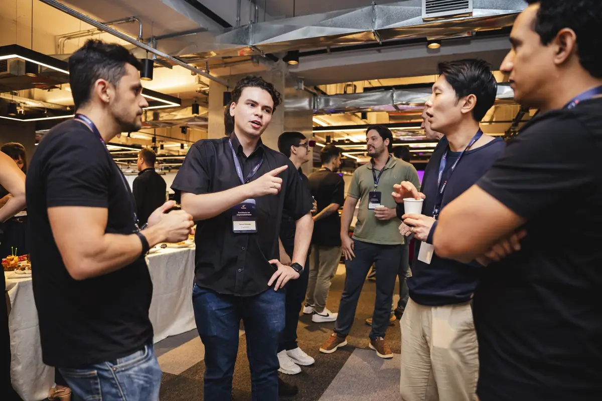Grupo de homens conversando em evento empresarial com crachás e bebidas