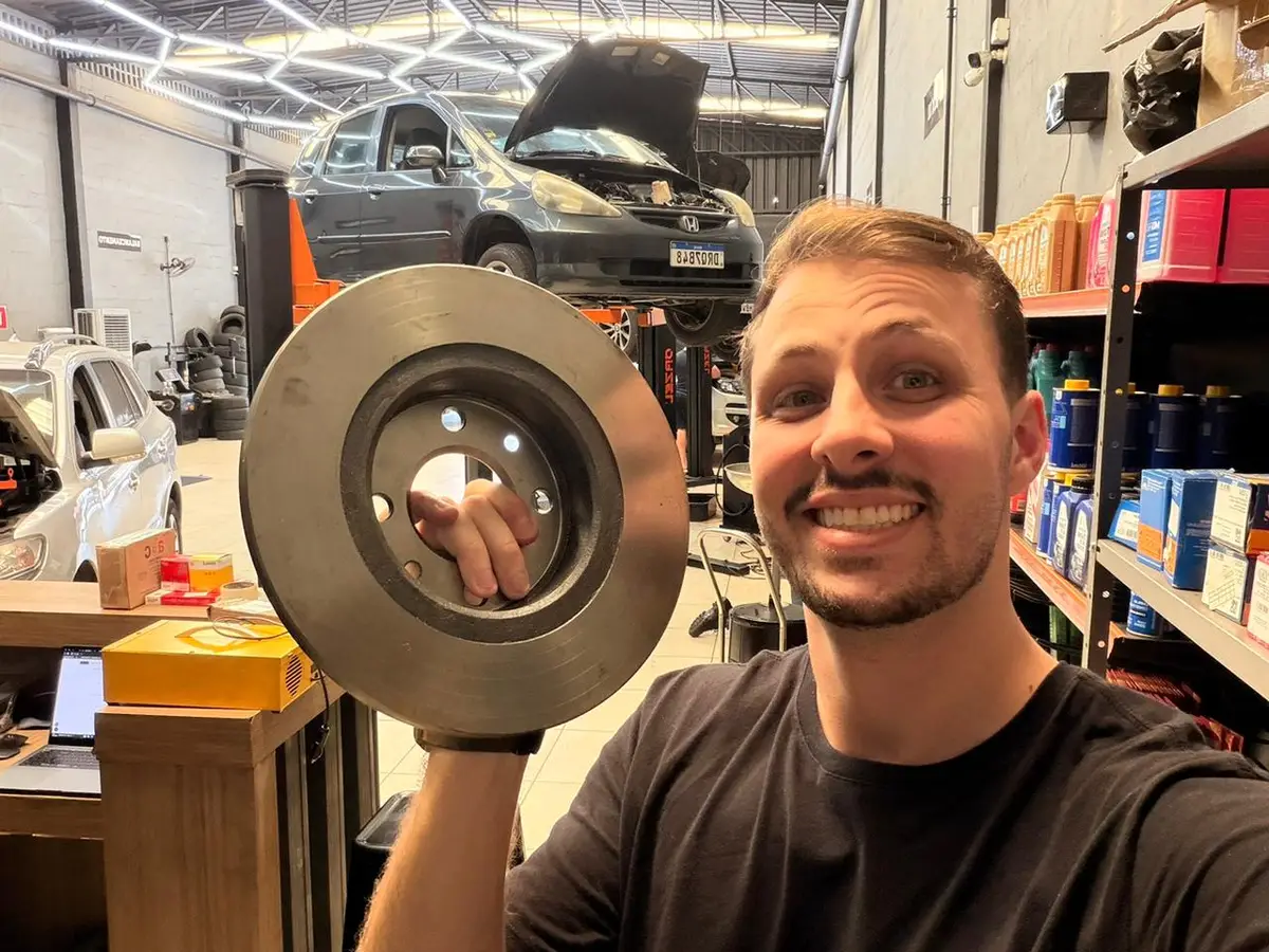 Homem sorridente segurando disco de freio em oficina automotiva moderna