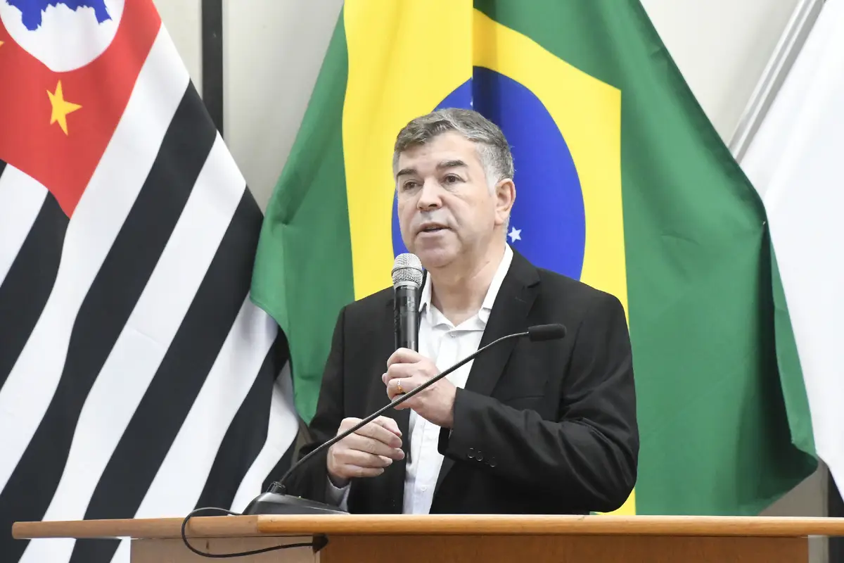 Homem falando ao microfone em um púlpito com bandeiras do Brasil e São Paulo ao fundo