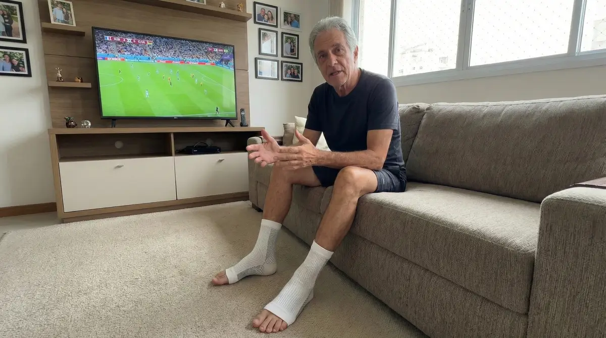 Homem sentado em sofá cinza usando meias de compressão NeuroFit com os dedos dos pés à mostra