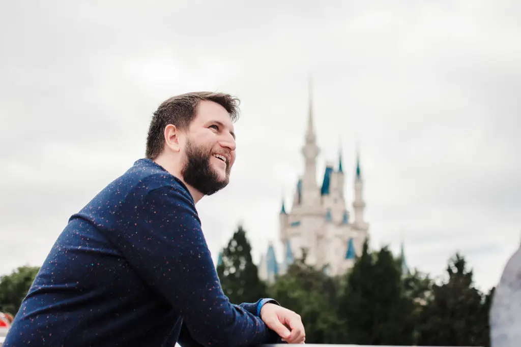 Homem sorridente com camiseta azul em frente ao Castelo da Cinderela na Disney em dia nublado