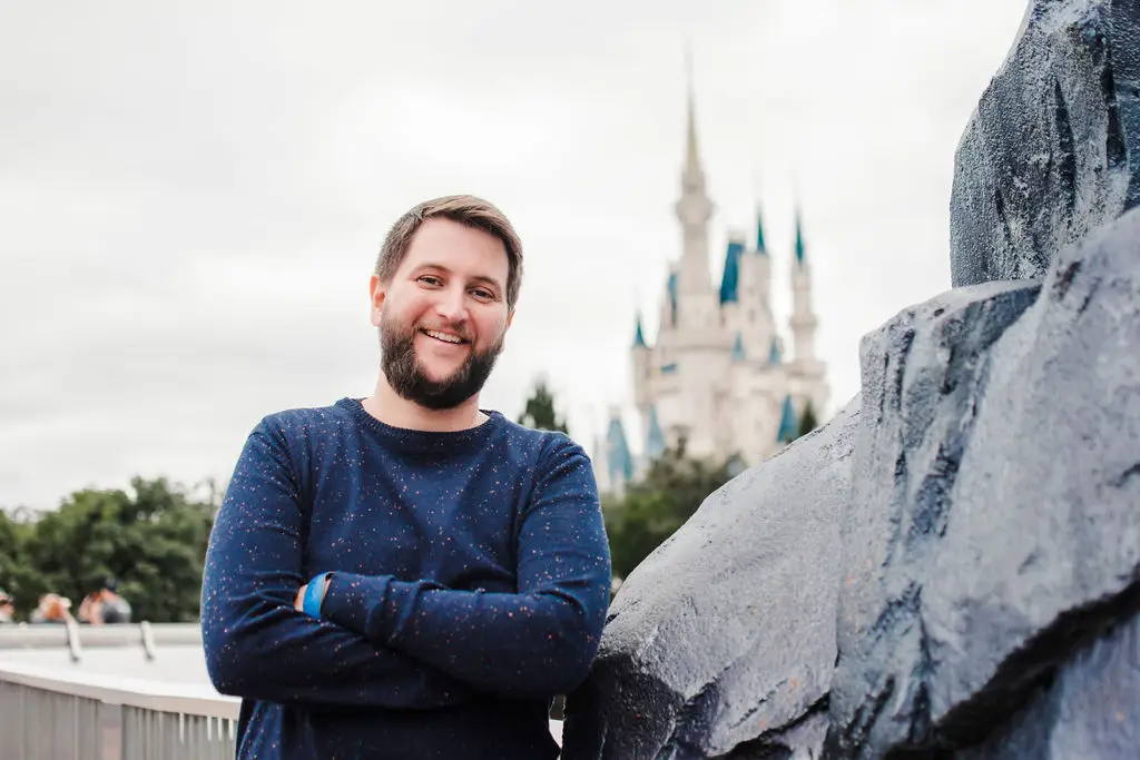 Homem sorridente com camiseta azul em frente ao castelo da Disney