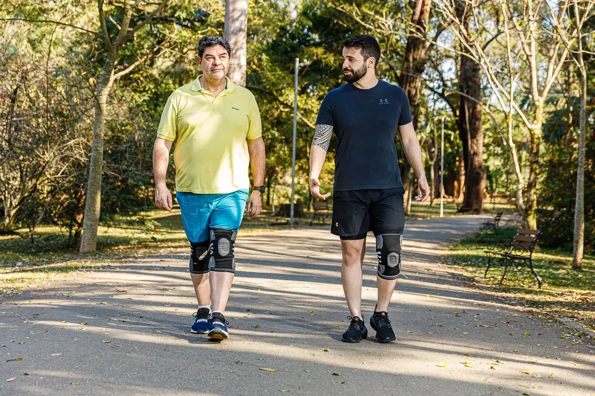 Dois homens caminhando em parque usando joelheiras de compressão nos joelhos